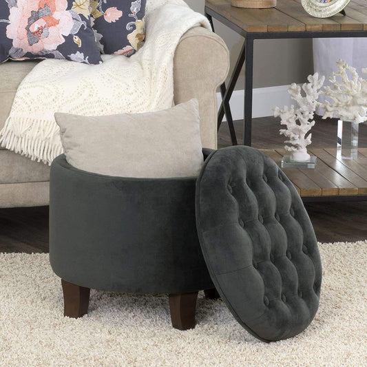 Gray tufted ottoman with a cushion on a beige carpet in a living room setting.