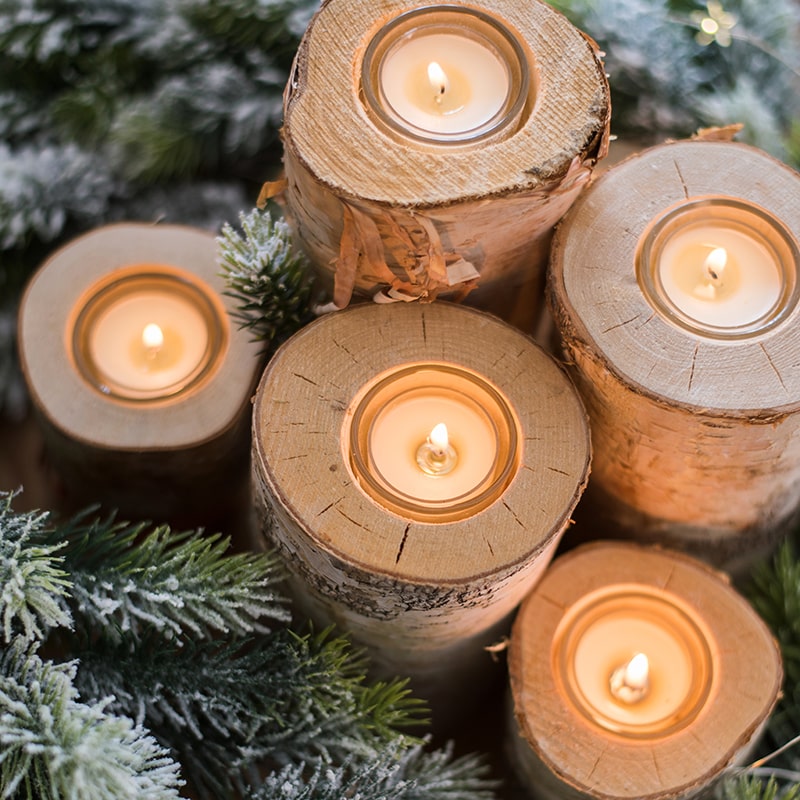 Wooden candle holders with lit candles surrounded by greenery