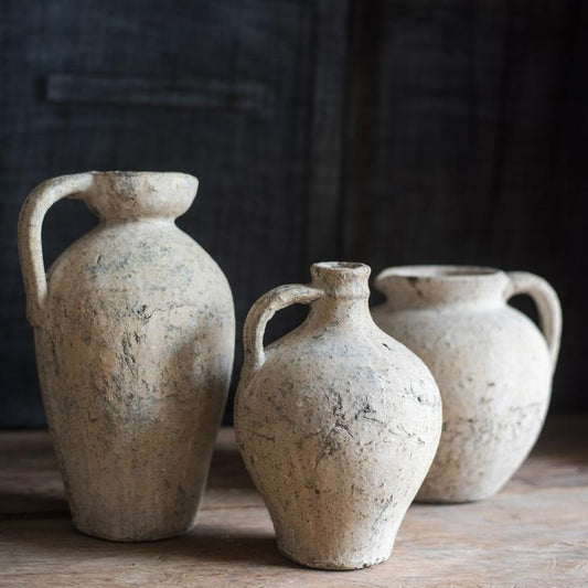 Three rustic clay jars with handles on a wooden surface against a dark background