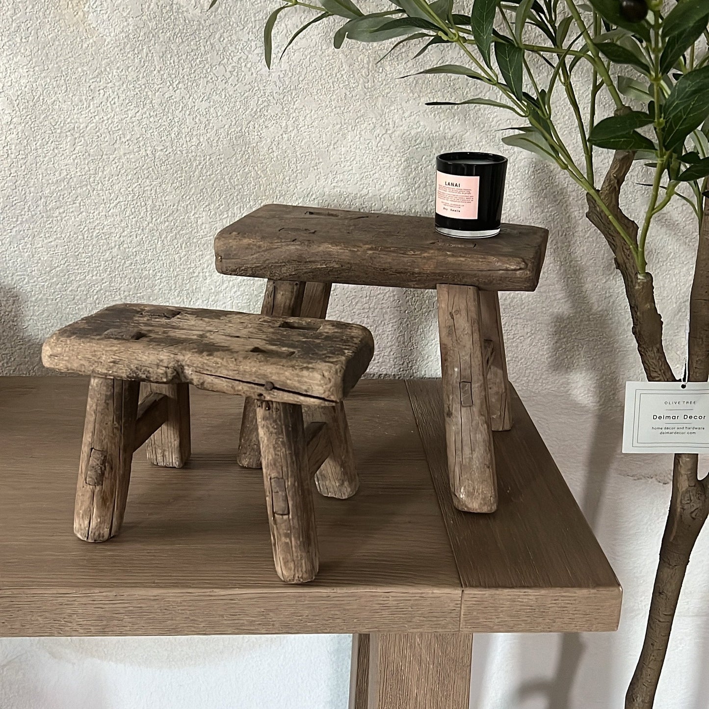 Two rustic wooden stools on a wooden surface with a candle and plant in the background.