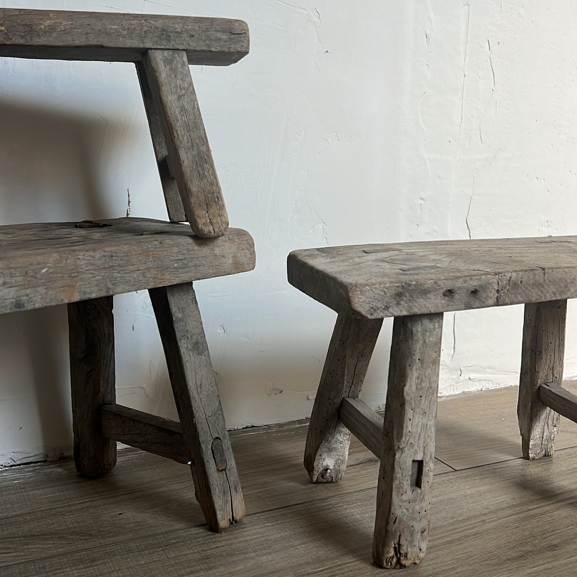 Two rustic wooden stools against a white wall.
