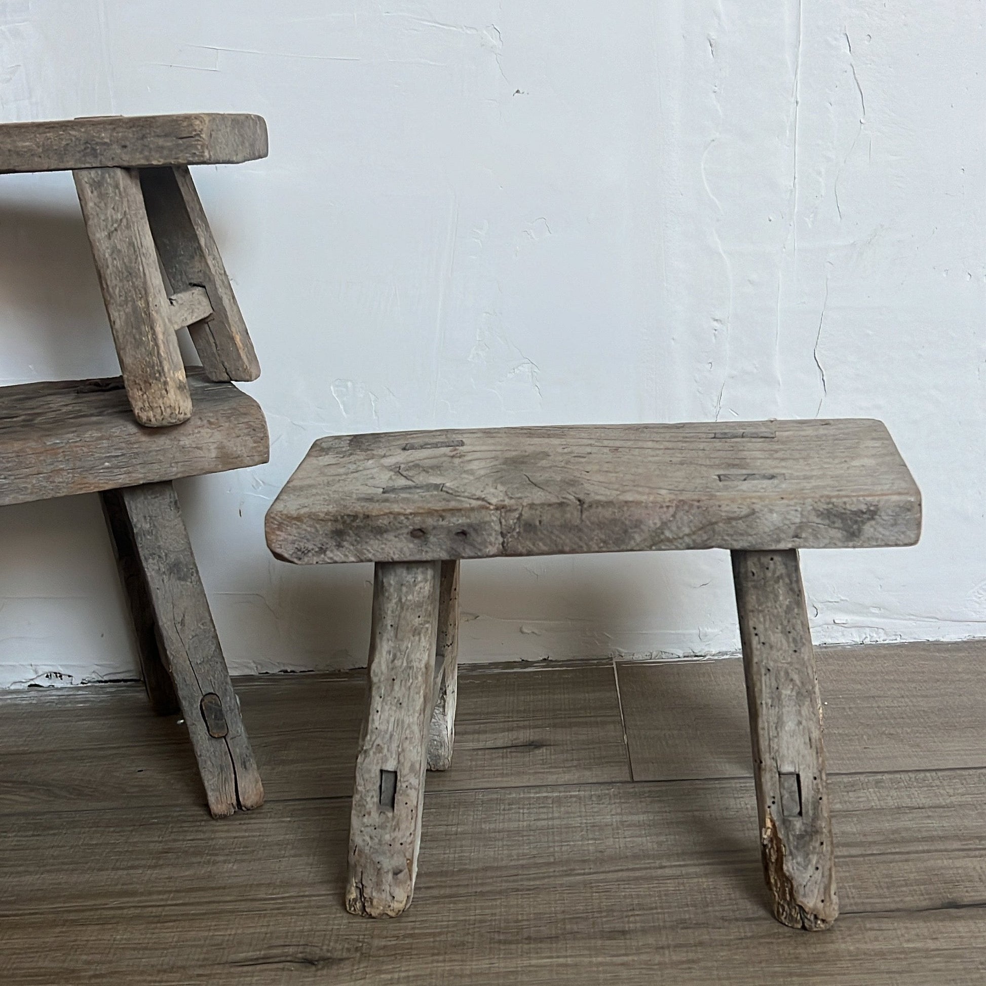 Two rustic wooden stools against a white wall.