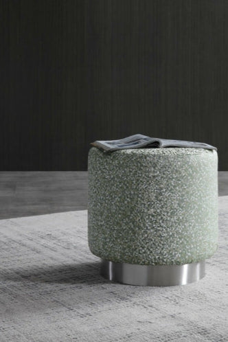 Green textured ottoman with metallic base on a gray rug against a dark wall