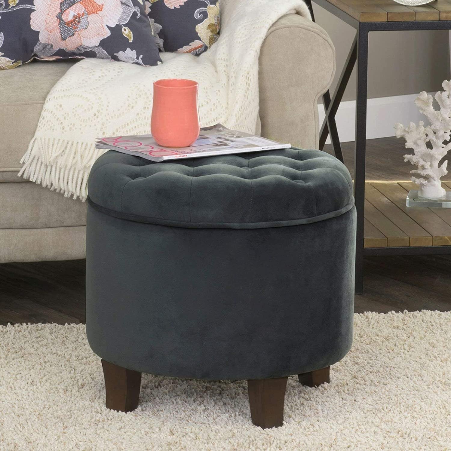 Gray tufted storage ottoman with a pink cup and magazine on top, in a living room setting.