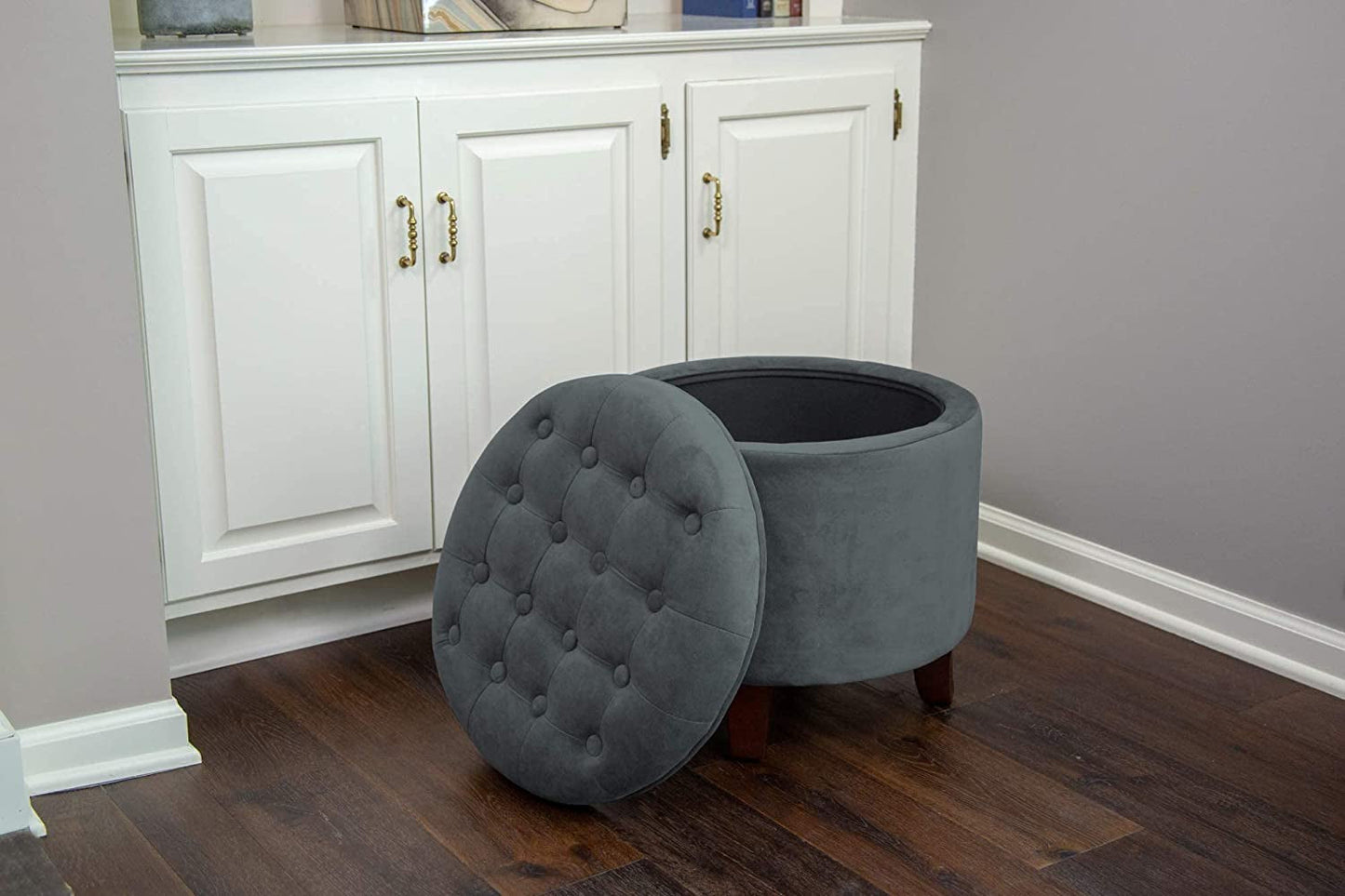 Gray tufted ottoman with storage compartment in front of a white cabinet.