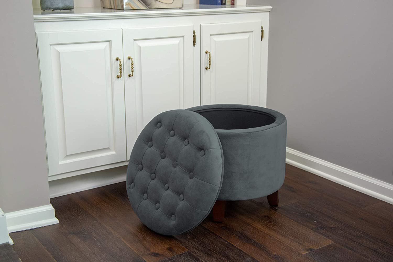 Gray tufted ottoman with storage compartment in front of a white cabinet.