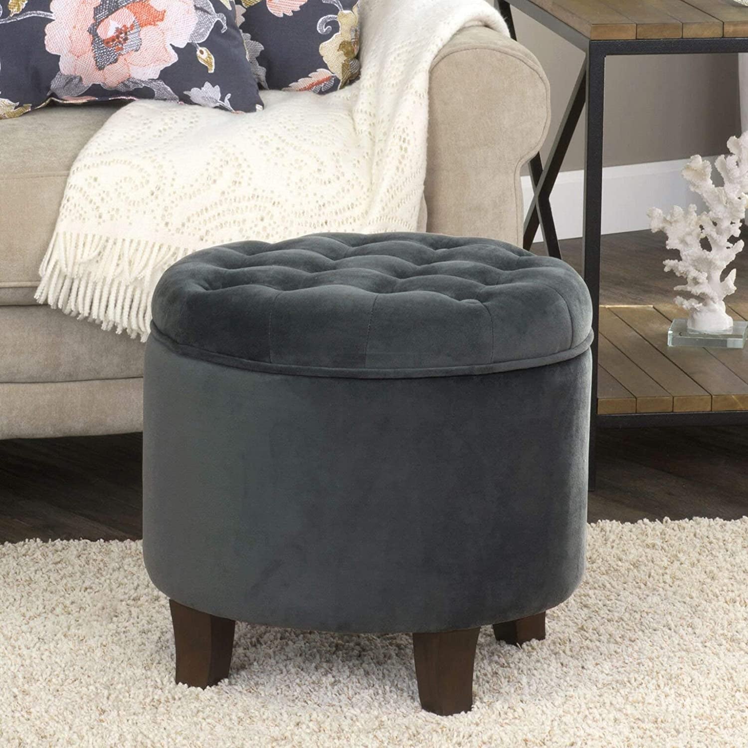 Gray tufted ottoman in a living room setting with a sofa and decorative pillows.