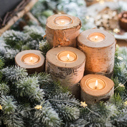Decorative candles in wooden holders on a bed of greenery