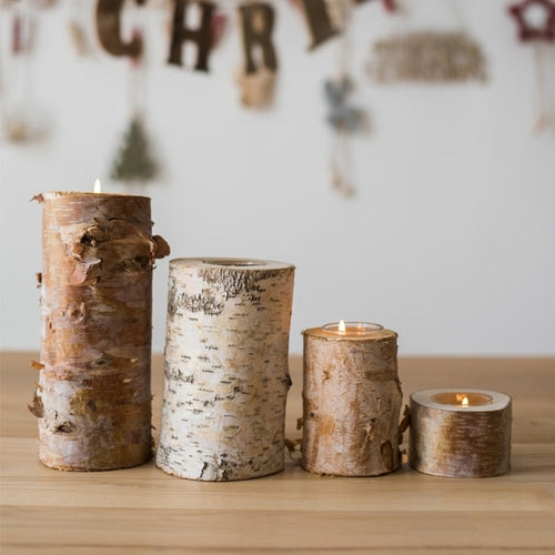 Birch bark candle holders with candles on a wooden surface, Christmas decorations in the background.