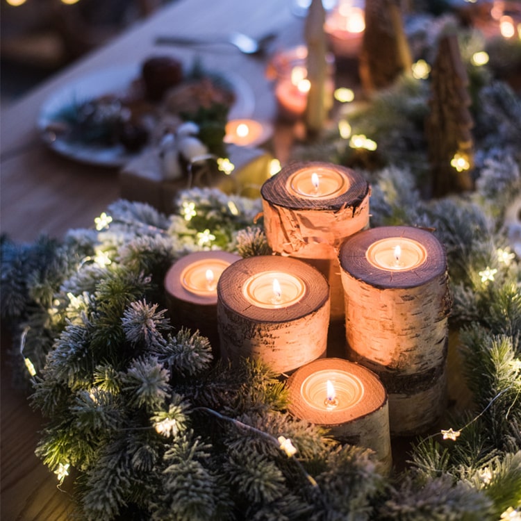 Decorative candles on birch logs surrounded by greenery and lights on a festive table.