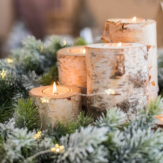 Decorative candles in birch bark holders on a bed of greenery with blurred background