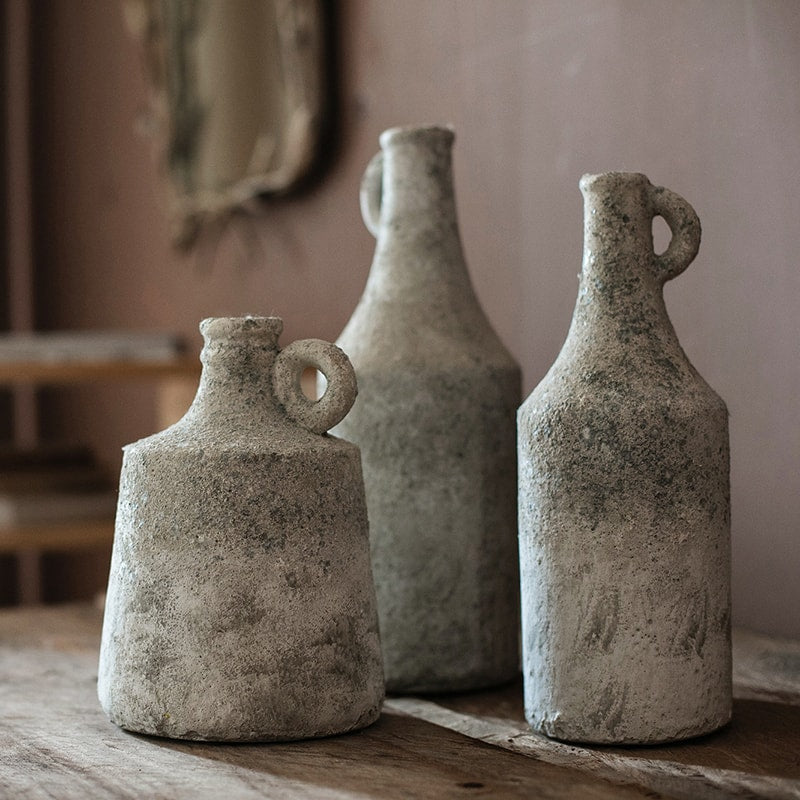 Three rustic stone vases on a wooden surface with a neutral background