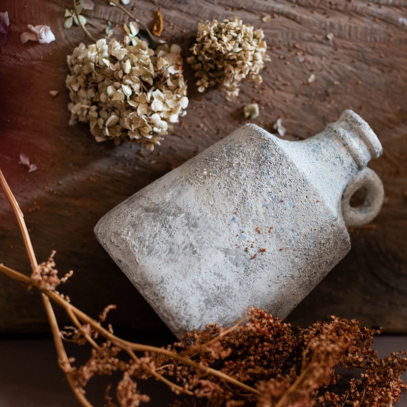 Vintage-style ceramic bottle on a wooden surface with dried flowers