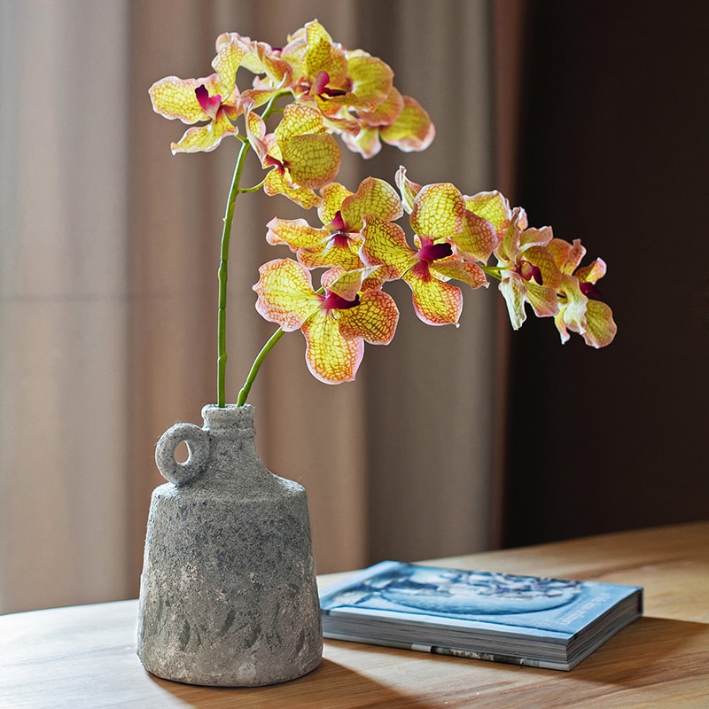 Decorative stone vase with a yellow orchid on a wooden surface.