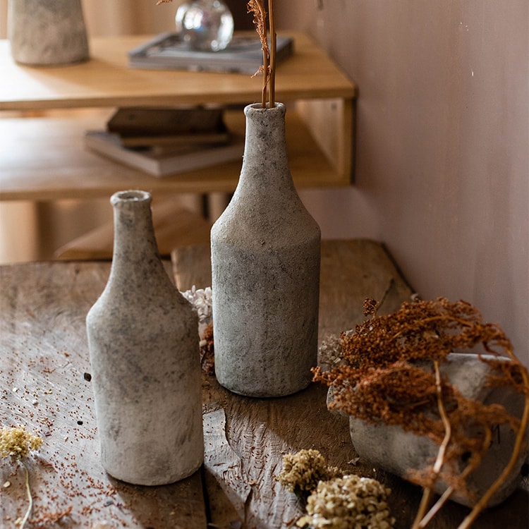 Two gray ceramic bottles on a wooden surface with dried plants.