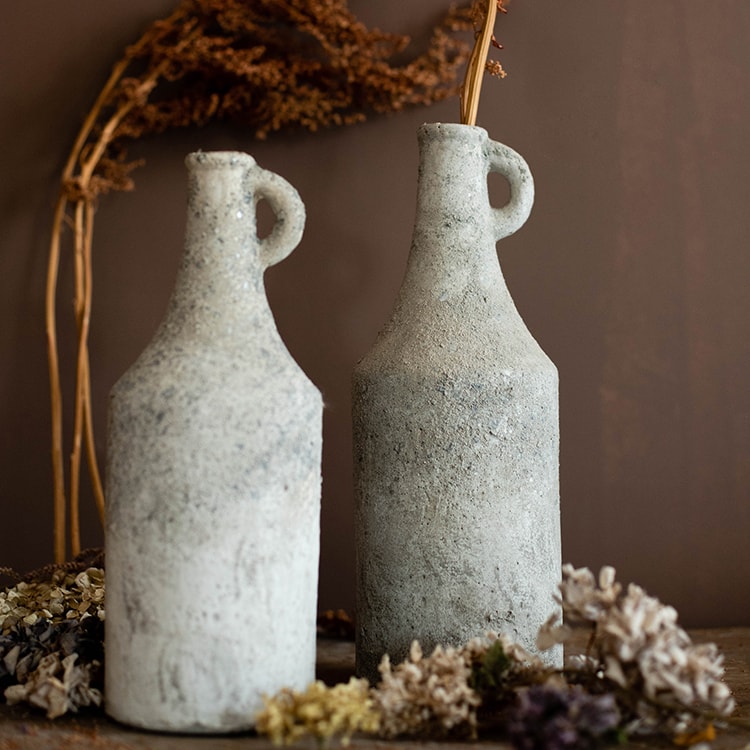 Two textured stone vases on a surface with dried plants and flowers.