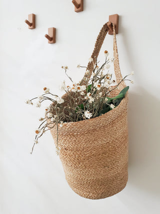 Woven basket with flowers hanging on a wall with wooden hooks.