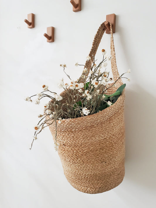 Woven basket with flowers hanging on a wall with wooden hooks.