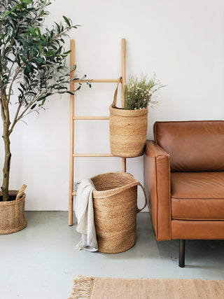 Living room with brown leather sofa, wicker baskets, and a ladder against a white wall.