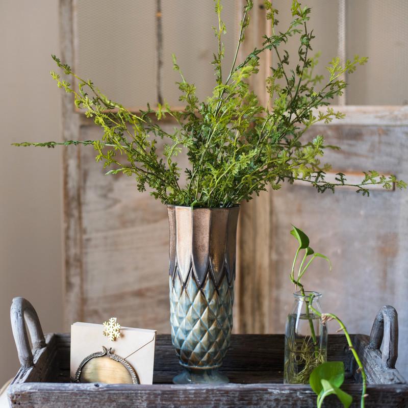 Decorative setting with a textured vase, greenery, and a wooden tray.