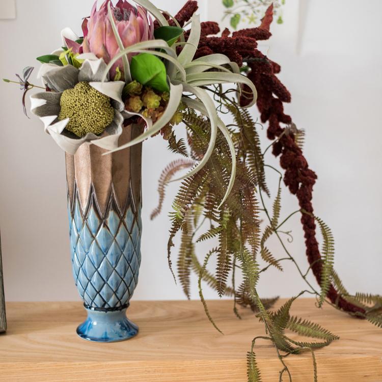 Decorative vase with a geometric pattern on a wooden surface, containing flowers and plants.