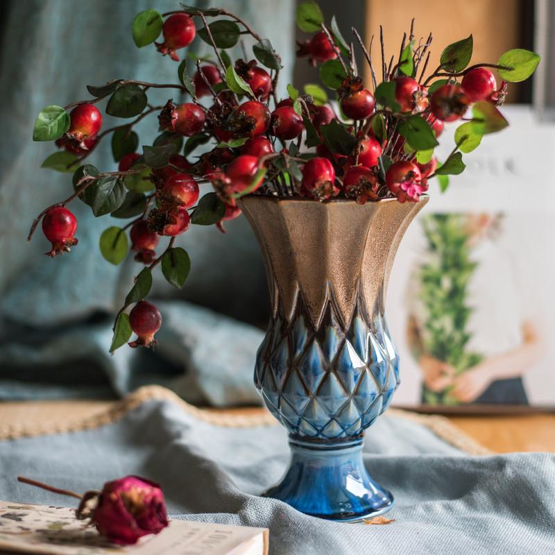 Decorative vase with red berries and green leaves on a soft surface
