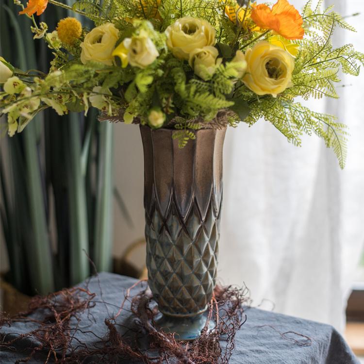 Decorative vase with a textured pattern holding a bouquet of yellow and green flowers on a table.