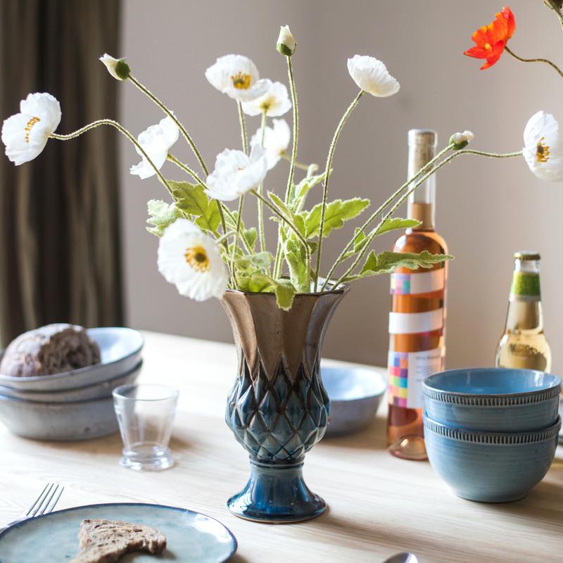 Vase with white flowers on a table with bowls and bottles in the background