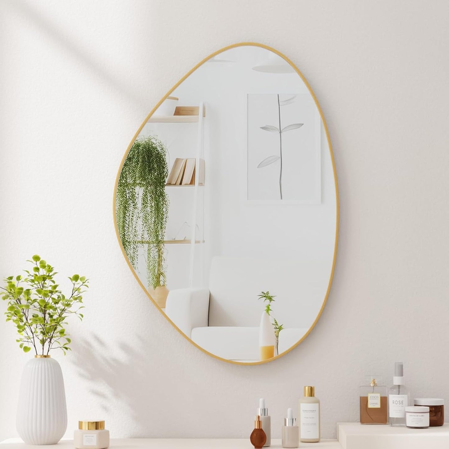 Round mirror with gold frame on a white wall with decorative items below.