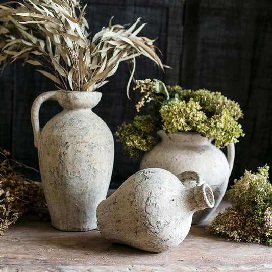 Three rustic clay vases with dried plants on a wooden surface