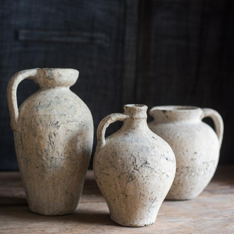 Three rustic clay jars with handles on a wooden surface against a dark background
