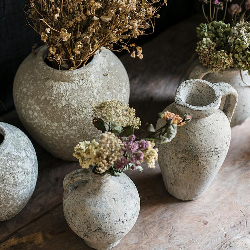 Collection of rustic stone vases with dried flowers on a wooden surface