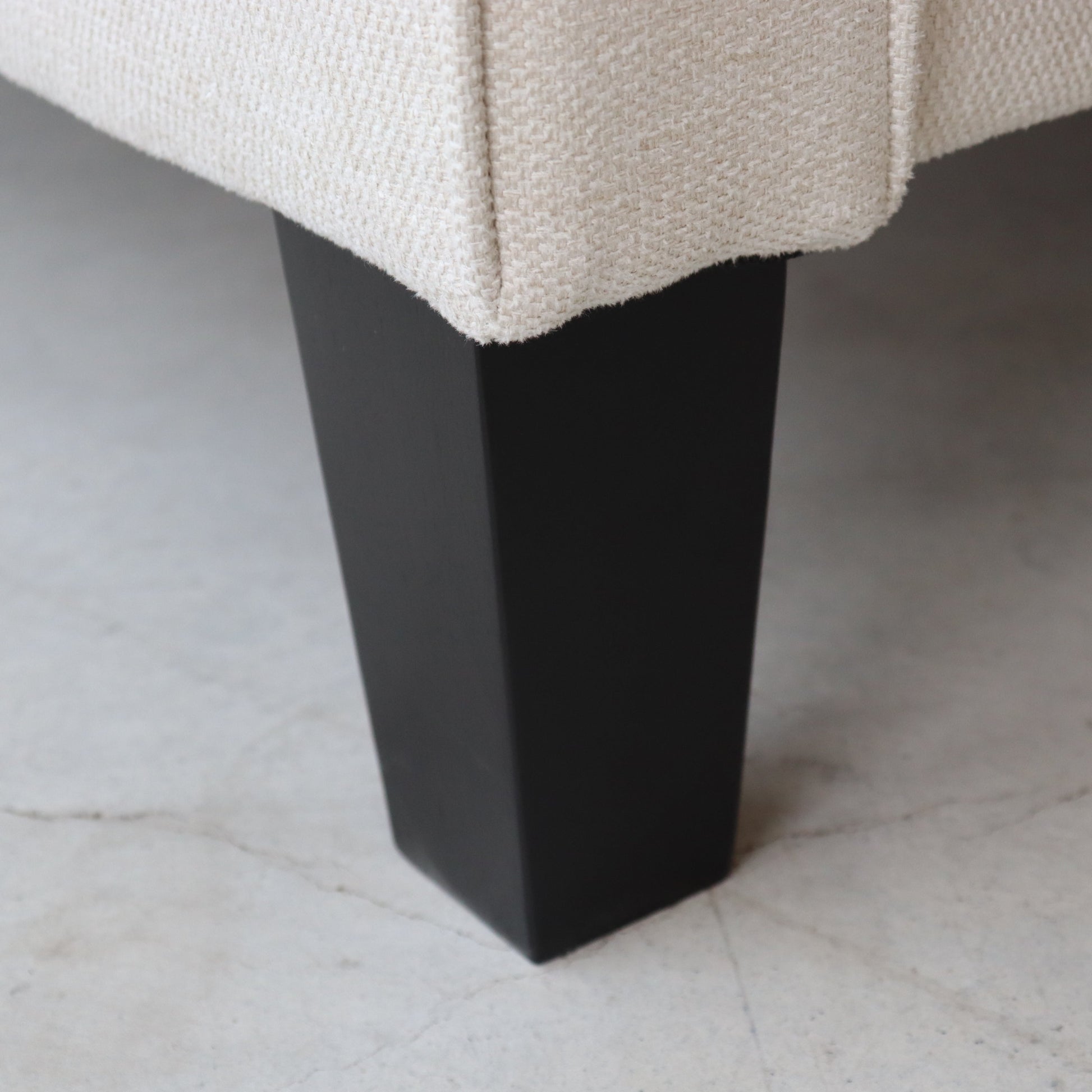 Close-up of a black furniture leg on a beige textured surface