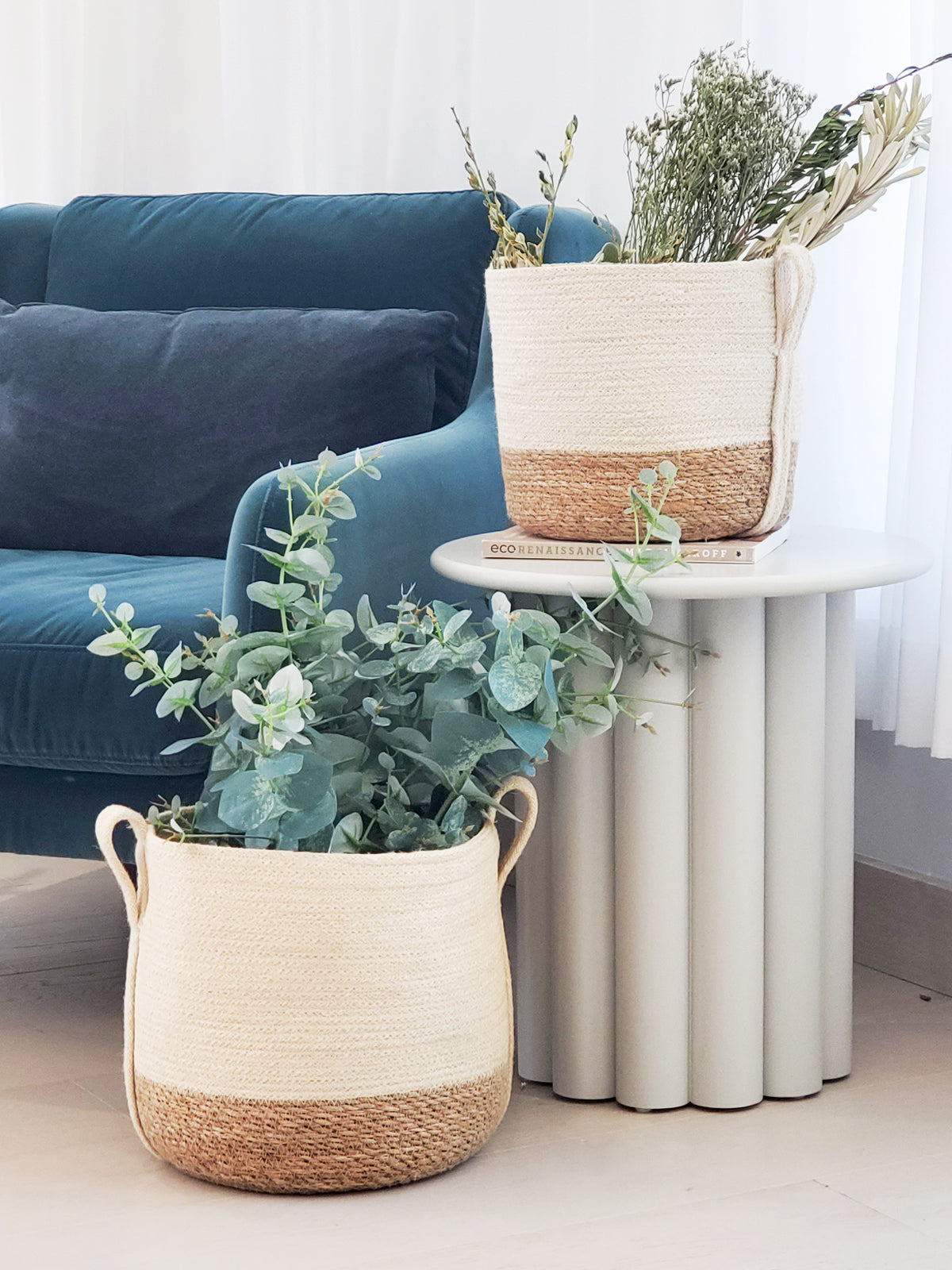 Decorative planters with greenery on a white surface, with a blue sofa in the background.