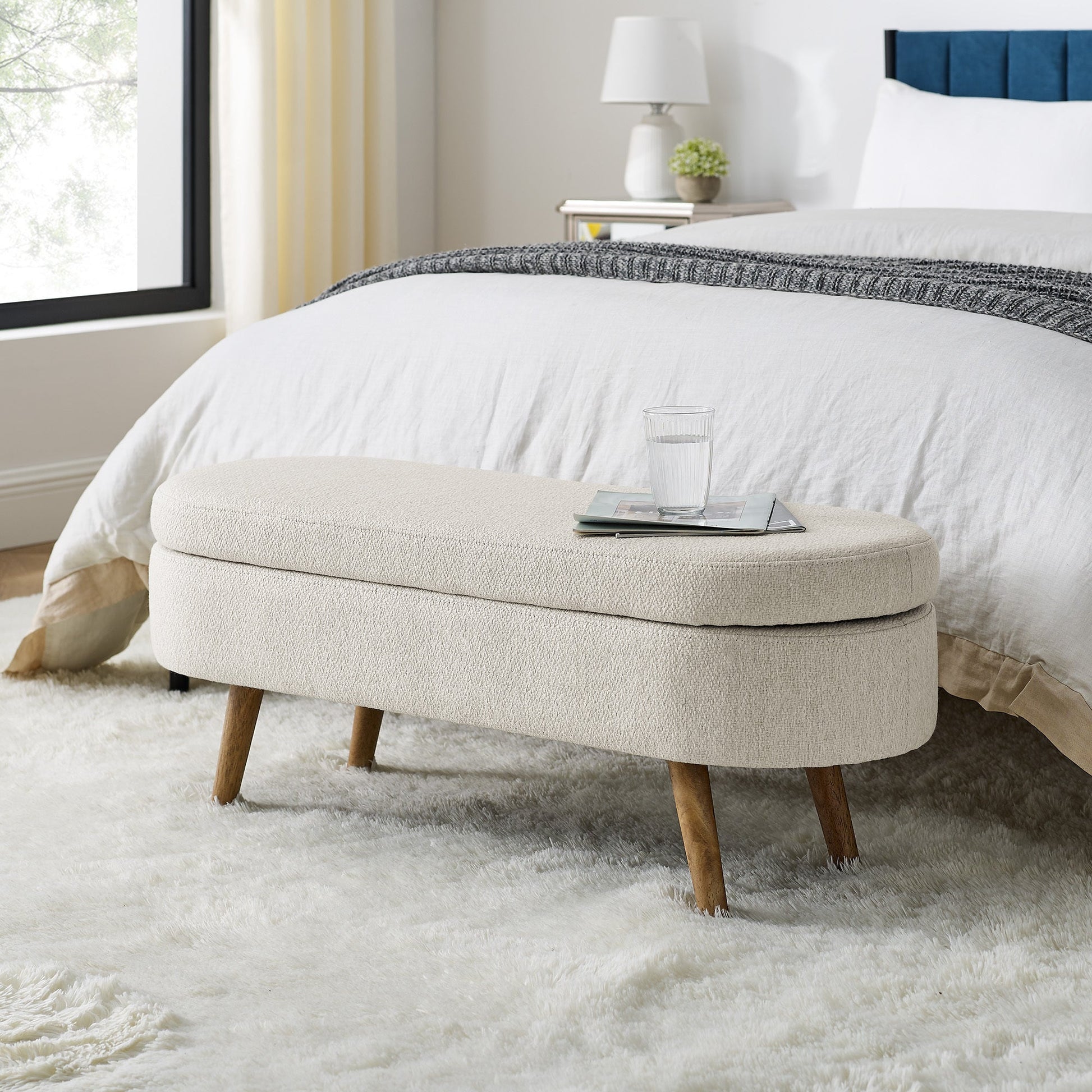 Beige ottoman with wooden legs in a bedroom setting