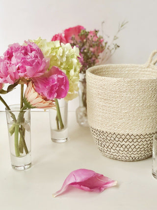 Floral arrangement with pink and green flowers in clear vases on a white surface, with a woven basket in the background.